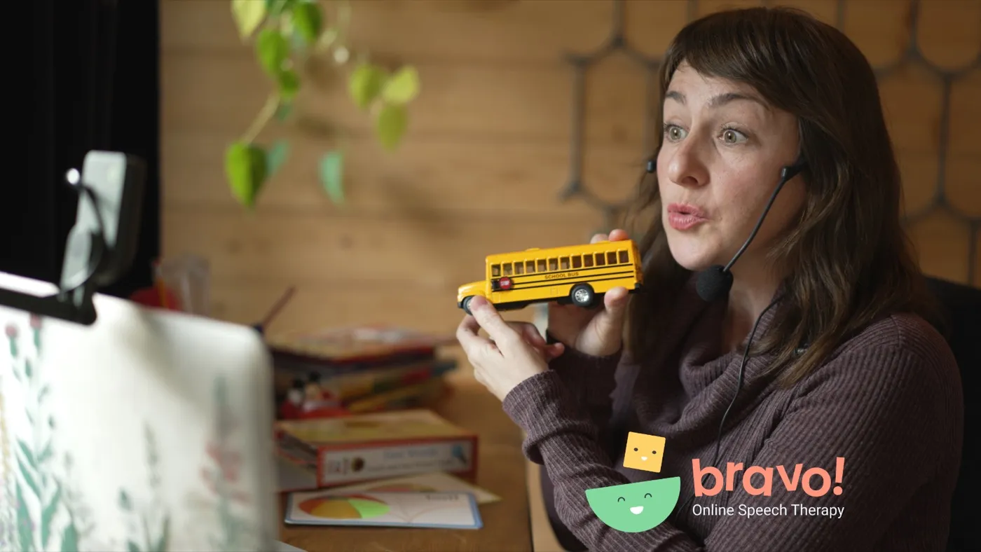 Heather mid-session over video, holding a toy school bus toward the camera